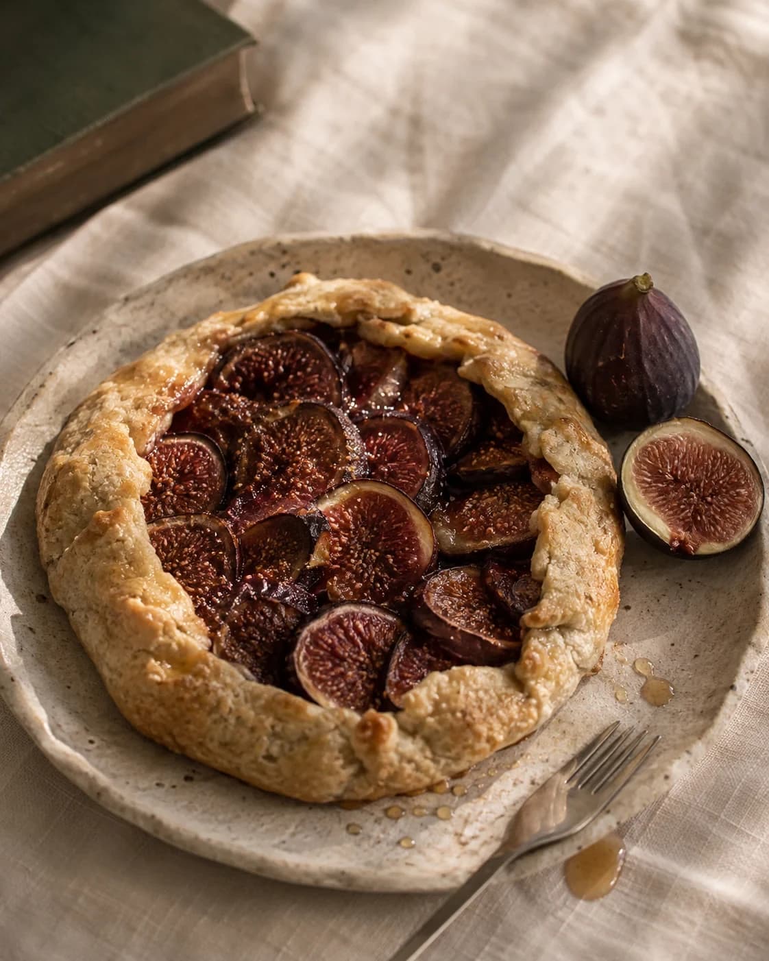 A rustic golden fig galette on a ceramic plate with fresh figs, linen and a fork.